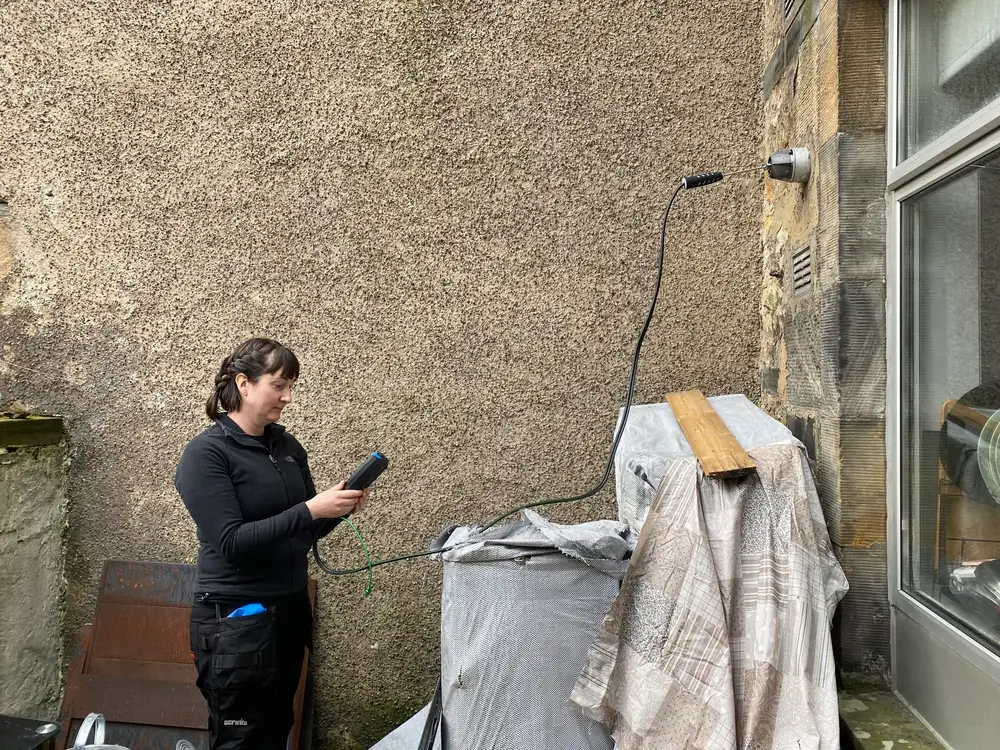 Rachel drilling through an outside wall for new pipework